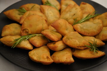 Golden-brown, half-moon shaped greens and herbs pies are arranged on a dark plate. They are...
