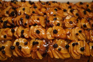 Close up of slices of glazed apple pie topped with raisins arranged neatly in a grid pattern. The pie features golden brown apple slices, caramelized for a glossy finish.  