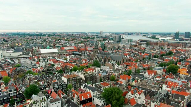 Drone shot over Amsterdam city center with Oude Kerk, traditional Dutch architecture, red roofs, and canal layout. Perfect for travel, tourism, and urban heritage content. 4K establishing aerial view