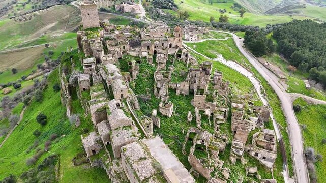Aerial view of an ancient, abandoned stone village of Craco, Italy on a hill under a cloudy sky.