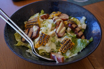 Close-up of a fresh Caesar salad topped with grilled chicken breast, charred corn, crunchy croutons and creamy dressing, served in a ceramic bowl on a wooden table. Healthy and flavorful gourmet lunch