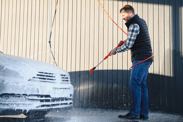 A man washes off the foam while washing the car. A vehicle is engulfed in soapy foam during a car...