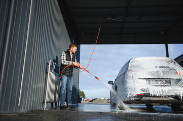 Car wash equipment. A man is washing a car at self service car wash. High pressure vehicle washer...