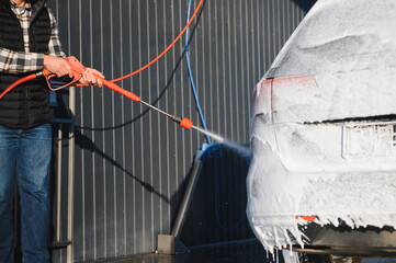 A man washes off the foam while washing the car. A vehicle is engulfed in soapy foam during a car...