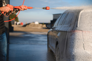 A man washes off the foam while washing the car. A vehicle is engulfed in soapy foam during a car...