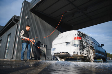 Car is washed at a professional car wash. Man washes a car with foam. Detailing