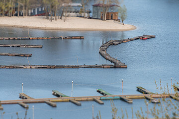Tranquil lakeside scene with small boats, dock, lifebuoys, muted colors, trees, buildings, daylight
