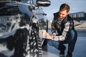 A man washes a car with a sponge at a self-service car wash