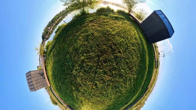 360&deg; tiny planet video transforming into a flat panoramic lakeside view. Modern cabins, sunrise reflections, and green landscape unfold as the camera smoothly rotates and unwarps the scene.