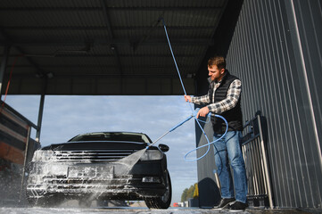 A man washes his car at a self service car wash using a hose with pressurized water.