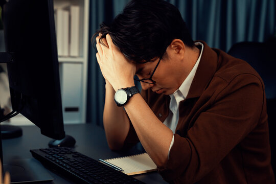 Smart businessman with stressful face working on pc waiting email from customer with making upper sales target revenue over late night time at office, working on startup company project job. Infobahn.