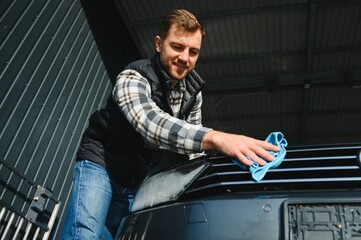 A man wipes his car with a microfiber towel after washing it at a car wash