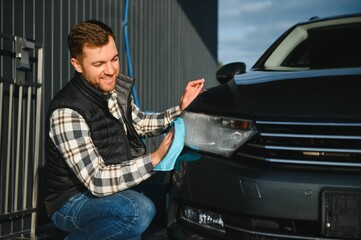 A man wipes his car with a microfiber towel after washing it at a car wash