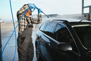 Man worker in uniform washing standing front car service station. Car wash cleaning station