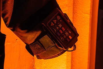 Hand holding a rugged radio communication device in dim, warmly-lit surroundings