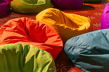 Colorful assortment of bean bag chairs in various hues on a patterned carpet, arranged casually for...