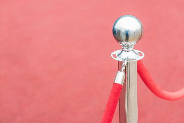 Red carpet, silver trophy on a rod, red velvet rope loop, possibly marking an exclusive area, gray background with subtle horizontal lines