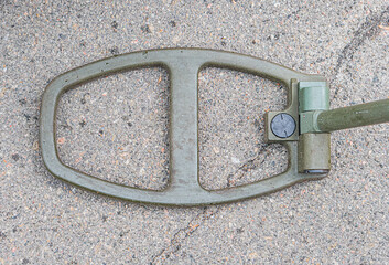 Old metal mine detector part on a concrete surface, exhibiting rust and handle-like structure with...
