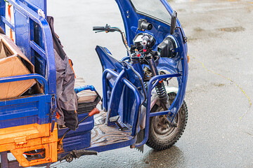 Electric cargo tricycle and motorbike, parked outside under overcast skies Blue courier van with...