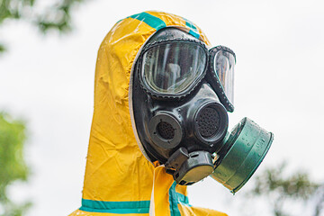 Person in yellow protective suit, hood, filter mask, goggles, outdoor environment, natural...