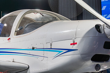 Single-engine white and blue aircraft with high tail structure, visible cockpit, indoors setting likely in an exhibition booth, bright lighting