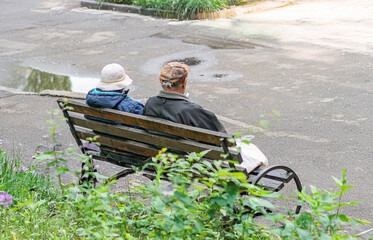 Outdoor scene, park bench, wood and metal, curved backrest, two individuals, straw hat,...