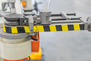 Industrial setting, large machine with platform or table, yellow and black striped tape cautionrestricted area marker, circular object possible pulley or axle, cylindrical components, electrical