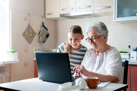 Child helping grandmother learning computer skills. Digital literacy, education and support. Kid and senior woman playing on laptop at home. Happy family moment. Technology lifestyle - Powered by Adobe
