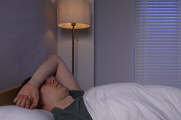 Frustrated man with alarm clock suffering from insomnia in bed indoors