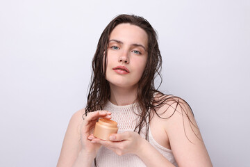 Portrait of beautiful woman with jar of skincare product on light grey background, closeup