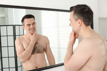 Smiling man after shaving looking at mirror in bathroom