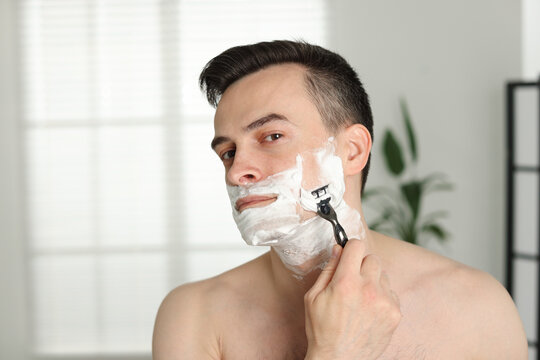 Handsome man shaving with razor at home - Powered by Adobe