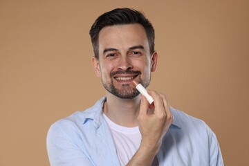 Smiling man applying lip balm onto his lips on light brown background