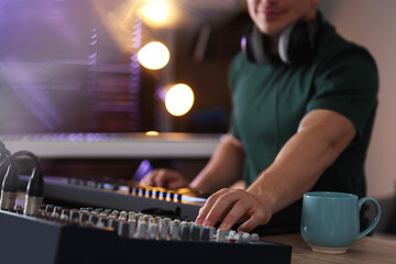 Man working with MIDI keyboard and dj mixer at table in home studio, selective focus