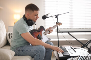 Man working with guitar and MIDI keyboard on sofa in home studio