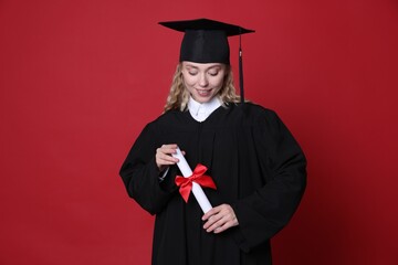 Happy student with diploma after graduation on red background