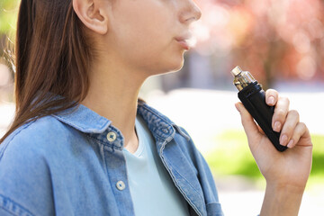 Young woman using electronic smoking device outdoors, closeup