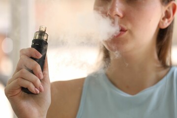 Young woman using electronic smoking device outdoors, closeup