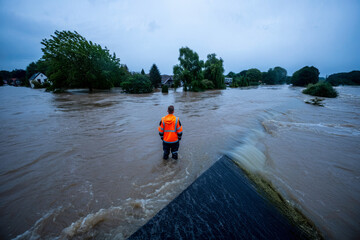 Flood rescuer stands in rising waters surveying submerged houses and trees under a stormy sky.