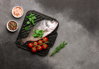 Raw dorado with spices, herbs and cherry tomatoes ready to grill on dark stone background top view....