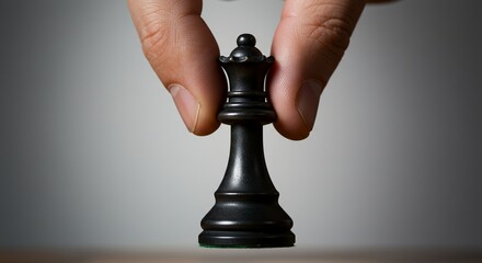 A hand holds a black chess queen against a neutral backdrop, suggesting strategic decision-making or a moment of choice.