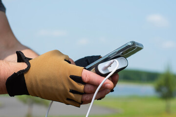Close-up of a person wearing half-finger cycling gloves, charging a smartphone with a power bank in nature. Concept mobility, active lifestyle, and technology on the go.