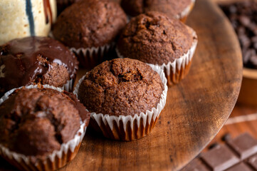 Chocolate muffins with liquid chocolate and dulce de leche with cocoa powder, a chocolate bar, and coffee beans on a wooden table with kitchen utensils.