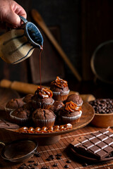 Chocolate muffins with liquid chocolate and dulce de leche with cocoa powder, a chocolate bar, and coffee beans on a wooden table with kitchen utensils.