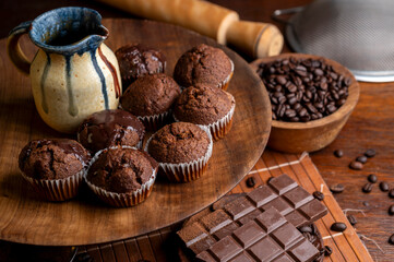 Chocolate muffins with liquid chocolate and dulce de leche with cocoa powder, a chocolate bar, and coffee beans on a wooden table with kitchen utensils.