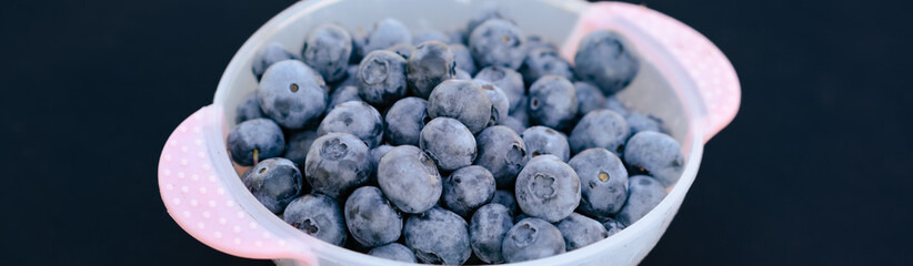 A large bowl brimming with fresh blueberries sits on a dark surface showcasing their vibrant blue color and inviting appearance for healthy eating and culinary uses
