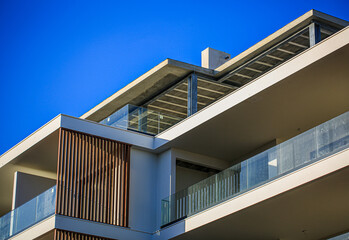 Modern apartment building with glass balconies, vertical wood panel accents, and unfinished rooftop...