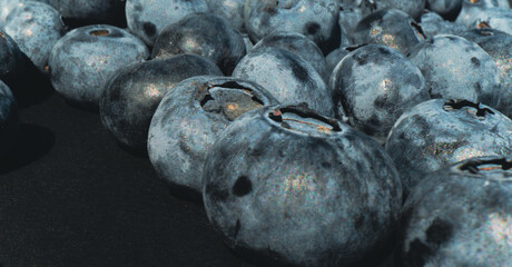 Clusters of freshly collected blueberries rest on a dark surface highlighting their vibrant hues...
