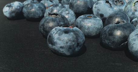 Clusters of freshly collected blueberries rest on a dark surface highlighting their vibrant hues and unique textures The sunlight illuminates their surfaces enhancing their appeal