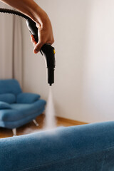Homemaker using steam cleaning machine, removing tough stains from upholstered blue couch in modern...